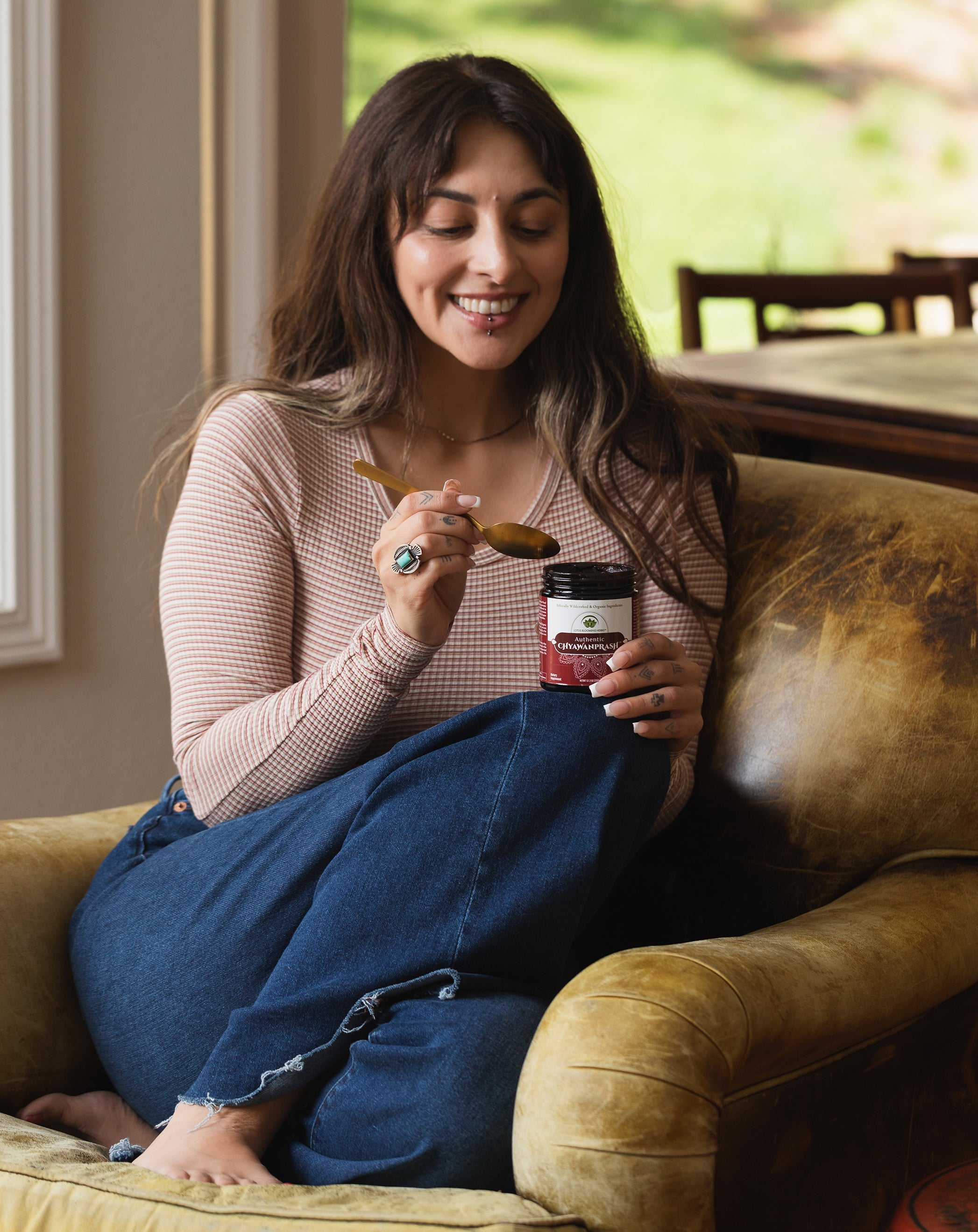 Woman sitting on a couch holding a jar of chyawanprash and a spoon.
