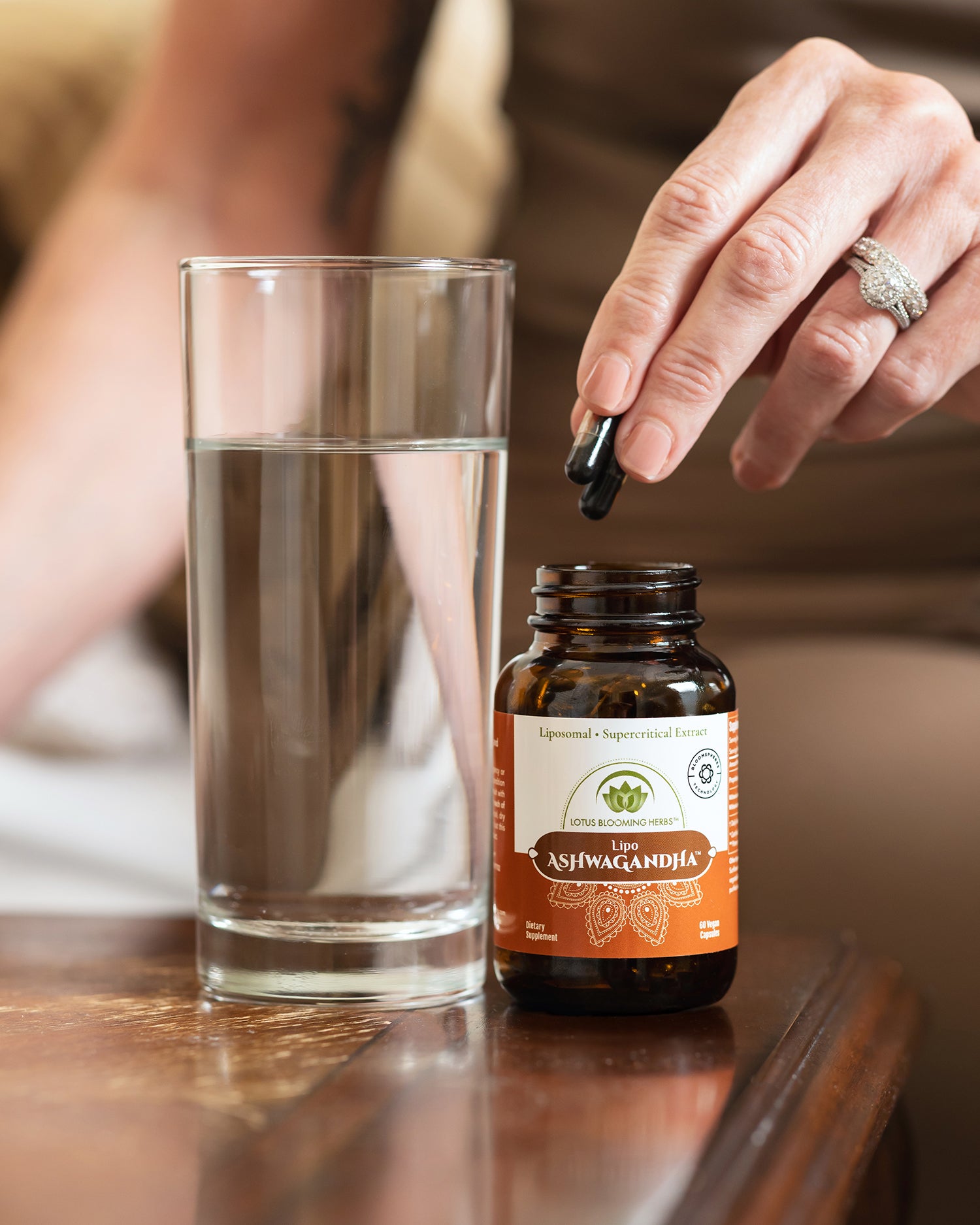 Person holding ashwagandha capsules next to a glass of water.