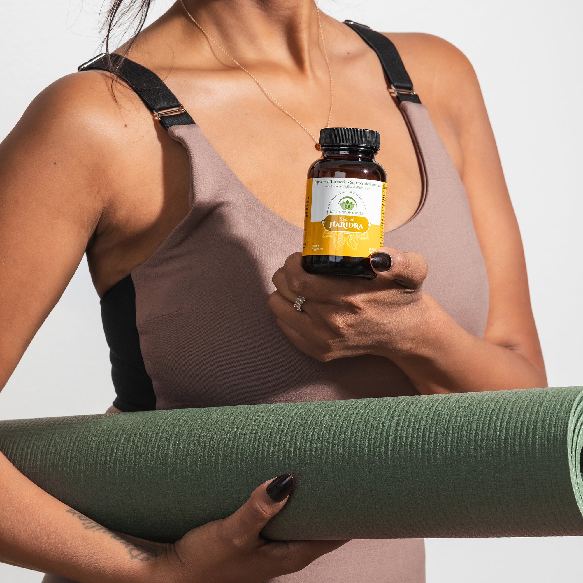 Woman holding a yoga mat and a turmeric supplement bottle
