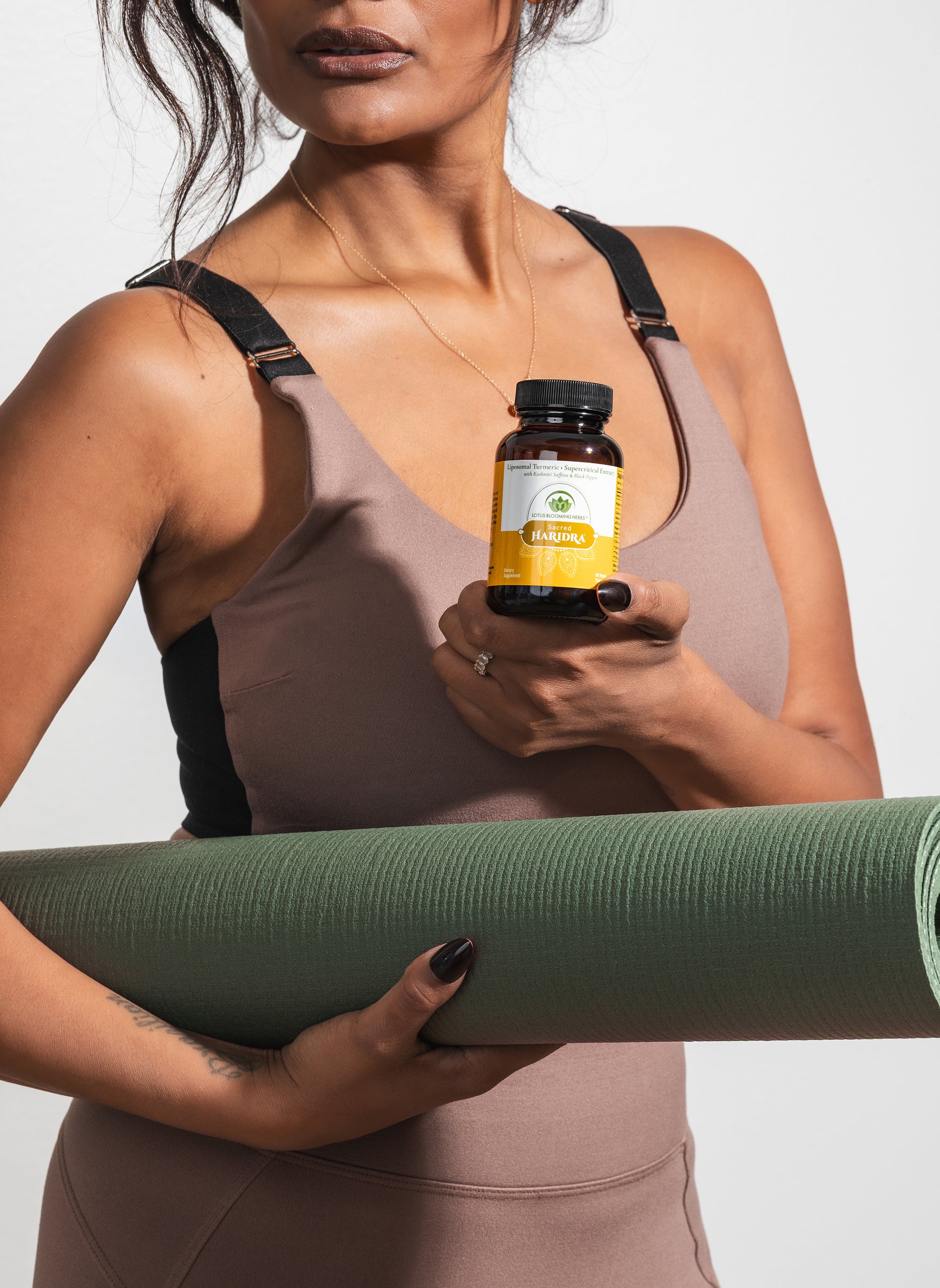 Woman holding a yoga mat and a turmeric supplement bottle